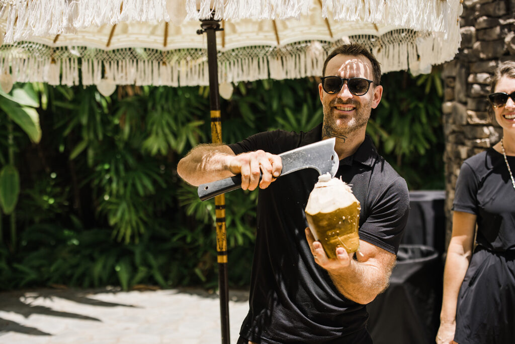 Matias Ezcurra Photography, Man expertly chopping a coconut at a Maui wedding, providing refreshing drinks for guests.