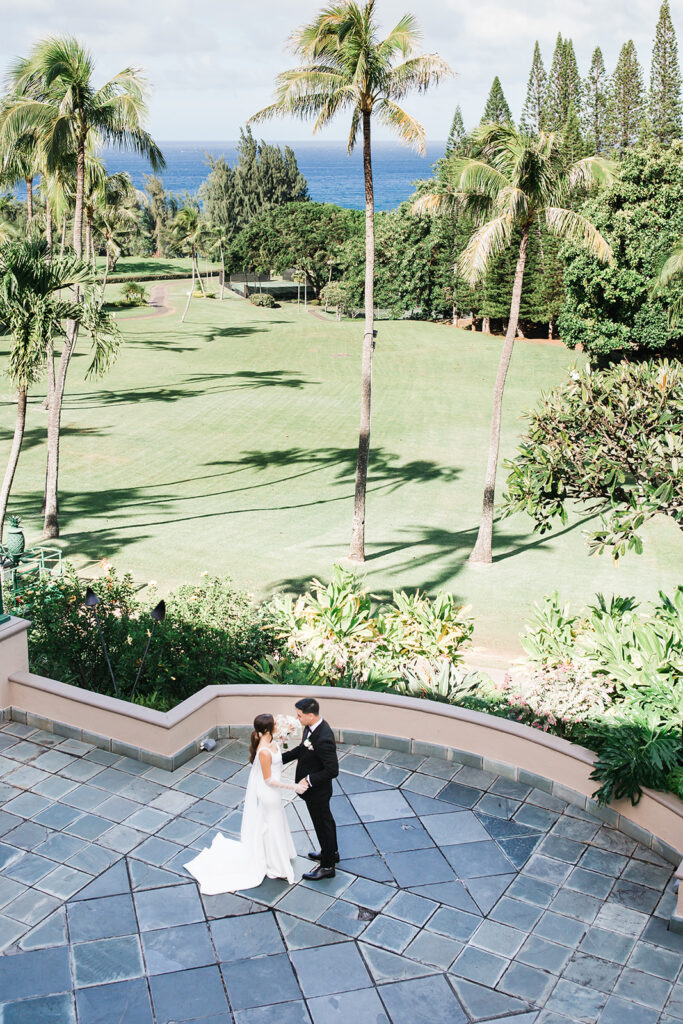 Matias Ezcurra Photography, Bride and groom embrace on a Ritz-Carlton Kapalua patio overlooking a manicured lawn and ocean.