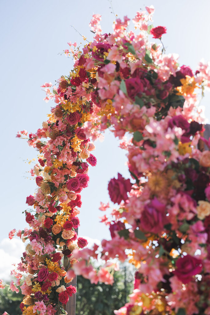 Matias Ezcurra Photography, Vibrant floral wedding arch at Hotel Wailea, featuring pink, red, and yellow blooms.