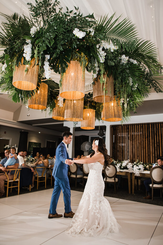 Matias Ezcurra Photography, Bride and groom dance under lush floral chandelier at luxury Maui wedding venue.