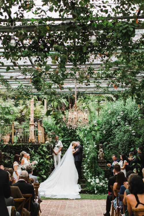Matias Ezcurra Photography, Bride and groom kiss at their Haiku Mill wedding ceremony, surrounded by lush greenery.