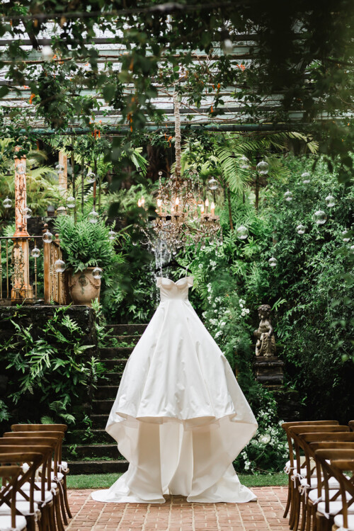Matias Ezcurra Photography, Elegant wedding gown displayed in a lush tropical garden setting at the Haiku Mill.