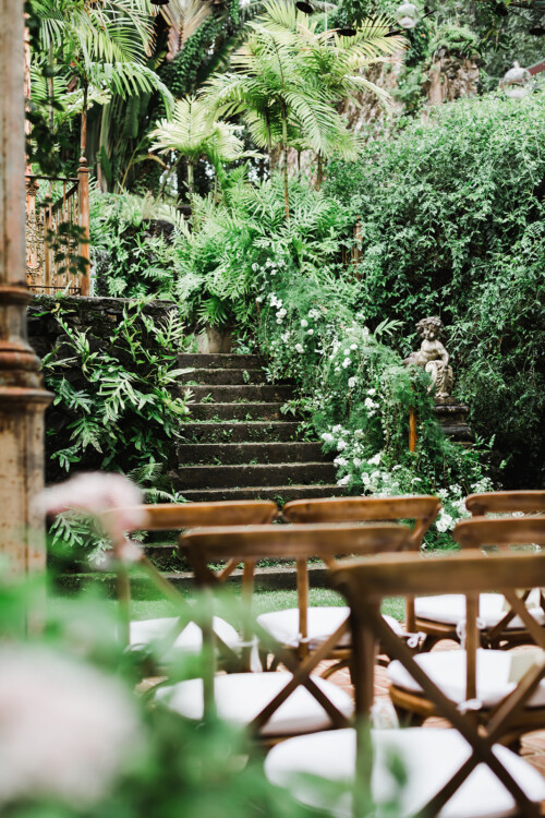 Matias Ezcurra Photography, Wooden chairs face a stone staircase adorned with greenery and flowers at a Haiku Mill wedding.