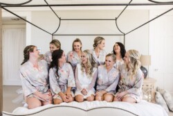 Matias Ezcurra Photography, Bride and bridesmaids in floral robes laugh together on a bed.