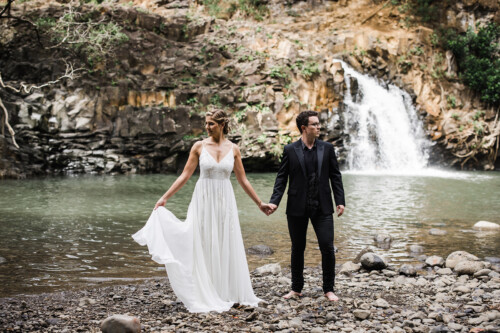 Matias Ezcurra Photography, Bride and groom holding hands by a waterfall at their wedding.
