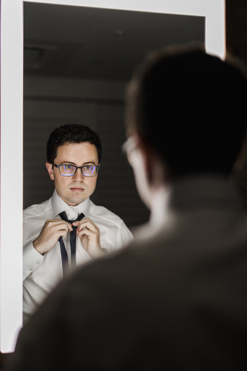 Matias Ezcurra Photography, Groom adjusting his tie in a mirror before Tim + Richelle's wedding.