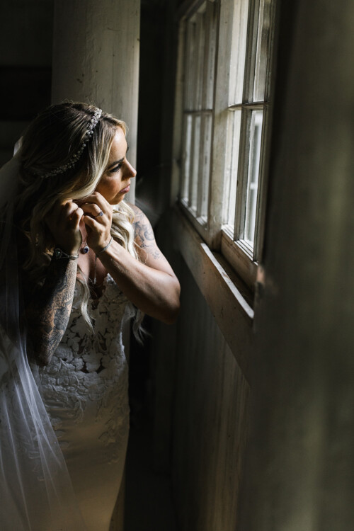 Matias Ezcurra Photography, Bride in lace wedding dress puts on earrings at Haiku Mill.