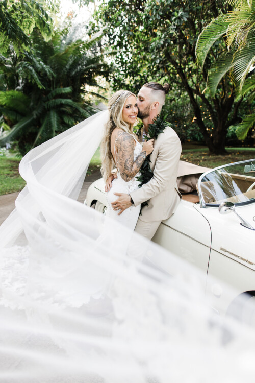 Matias Ezcurra Photography, Bride and groom embrace by vintage car at Haiku Mill wedding.