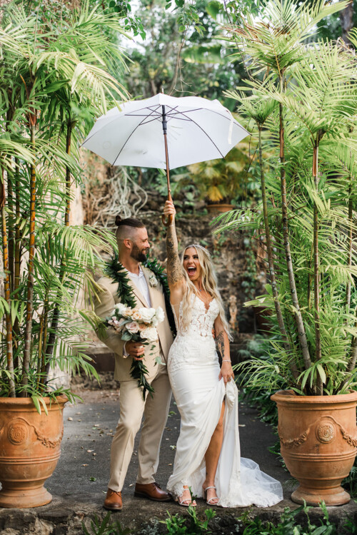 Matias Ezcurra Photography, Happy bride and groom share a laugh under a white umbrella at their Haiku Mill wedding.