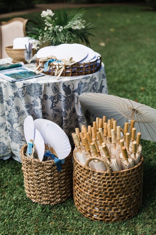 Matias Ezcurra Photography, White paper fans and parasols in wicker baskets at an Olowalu Plantation wedding.