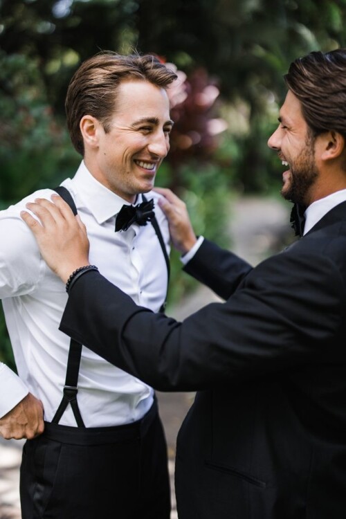Matias Ezcurra Photography, Two groomsmen laugh together at an Olowalu Plantation wedding. One adjusts the other's suspenders.