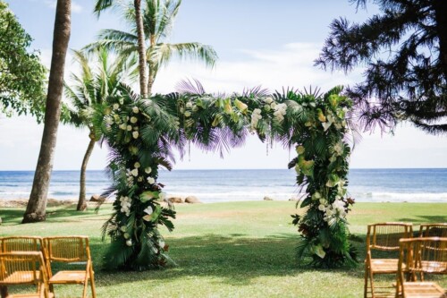 Matias Ezcurra Photography, Beach wedding ceremony arch decorated with lush tropical flowers and greenery at Olowalu Plantation.
