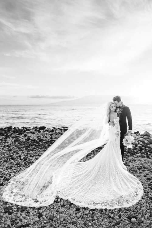 Matias Ezcurra Photography, Bride and groom embrace on Maui beach, Olowalu Plantation wedding. Long veil flows on rocks.