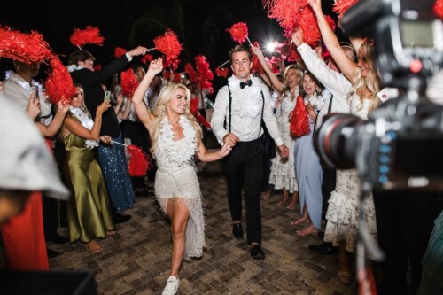 Matias Ezcurra Photography, Bride and groom joyfully exit their Olowalu Plantation wedding, guests cheering with red pom-poms.