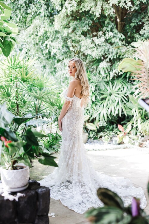 Matias Ezcurra Photography, Bride in off-the-shoulder lace wedding gown poses in tropical garden.