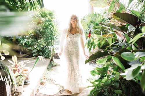 Matias Ezcurra Photography, Bride in lace wedding dress walking through lush tropical garden.
