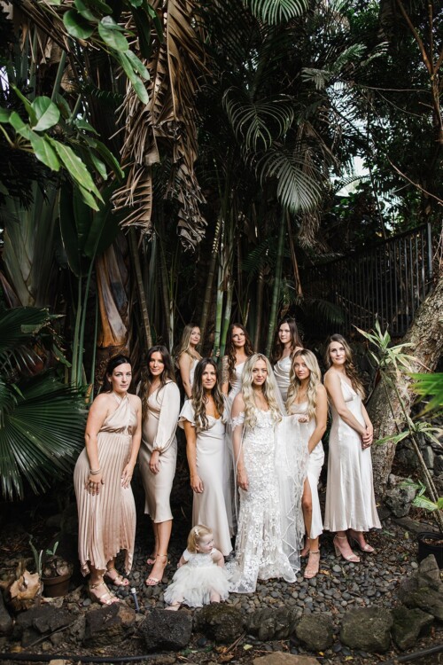 Matias Ezcurra Photography, Bride and bridesmaids in champagne-colored silk dresses pose for a photo in a lush tropical garden.