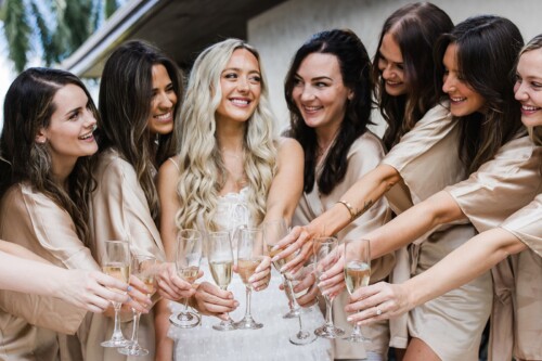 Matias Ezcurra Photography, Bride and bridesmaids in robes clinking champagne glasses in celebration