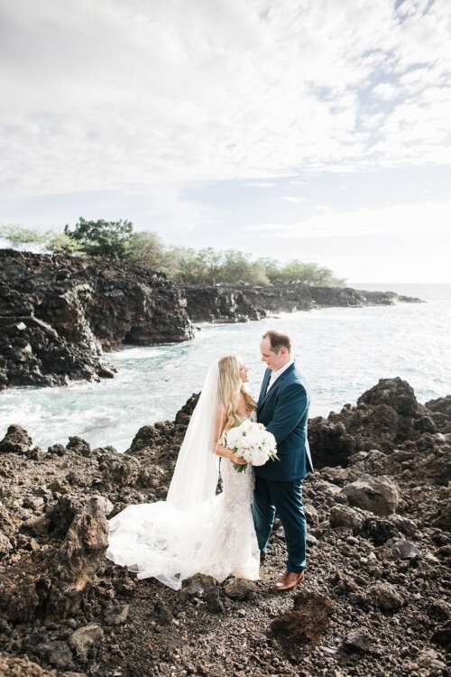Matias Ezcurra Photography, Bride and groom embrace on lava rocks near ocean, Hawaii wedding