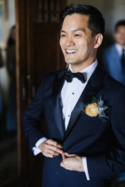 Matias Ezcurra Photography, Happy groom in navy tuxedo adjusts his jacket before his wedding.