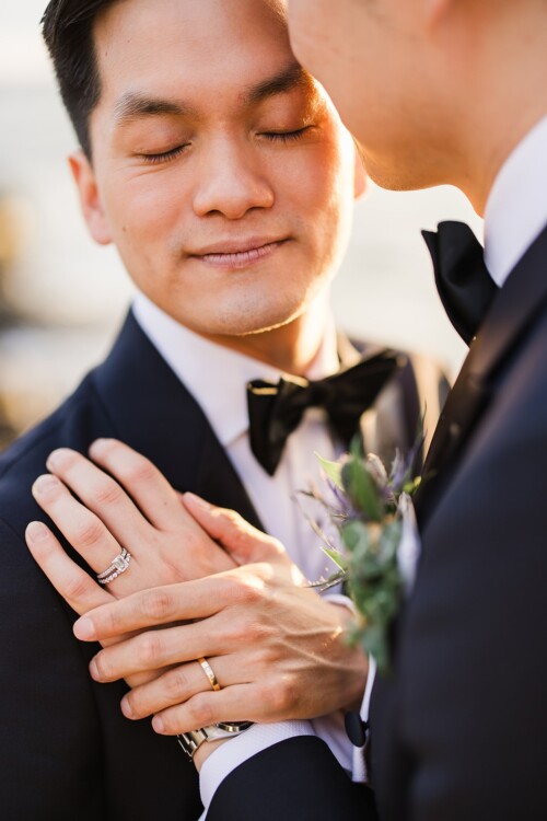 Matias Ezcurra Photography, Close-up of a gay couple embracing, one with eyes closed, wearing wedding rings and tuxedos.