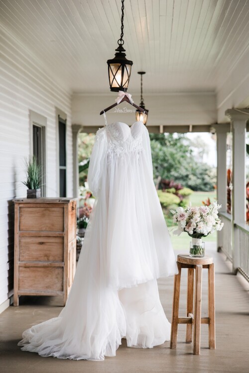 Matias Ezcurra Photography, Bride's wedding dress hangs on a porch at Olowalu Plantation House, next to bridal bouquet.