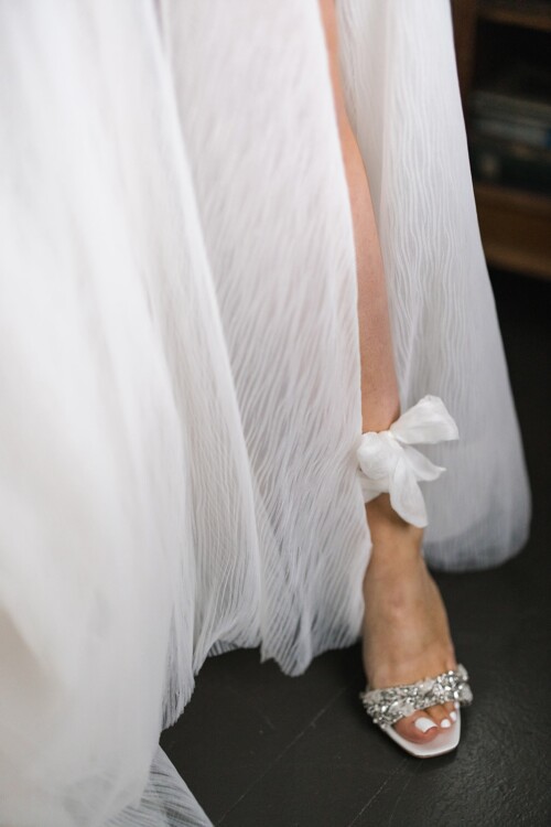 Matias Ezcurra Photography, Bride's feet in white wedding shoes with crystal embellishments, dress hem tied at ankle.