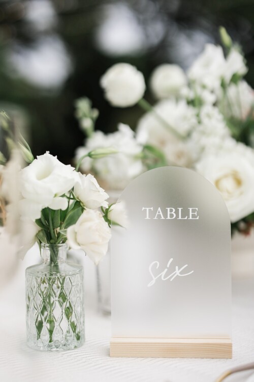 Matias Ezcurra Photography, Frosted glass table number six at a wedding reception with white flowers.