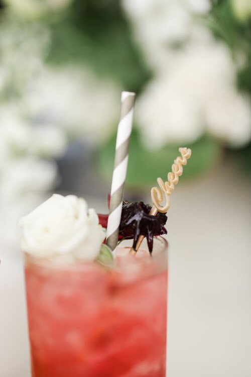 Matias Ezcurra Photography, Close-up of a refreshing pink cocktail garnished with a white rose, hibiscus, and a "Cheers" pick.