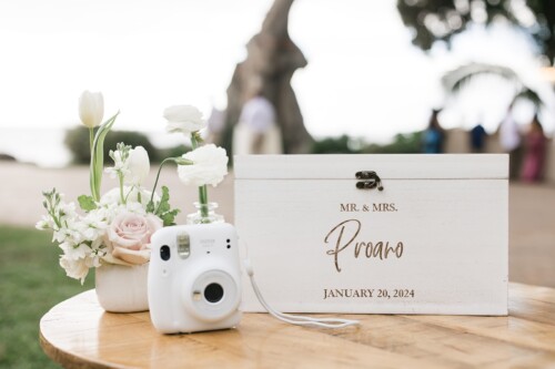 Matias Ezcurra Photography, White wedding guest book box with "Mr. & Mrs. Proano, January 20, 2024" engraved, Instax camera, and flowers.