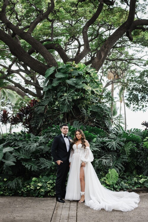 Matias Ezcurra Photography, Devan & David's wedding at Olowalu Plantation House, Maui. Bride and groom pose amidst lush tropical foliage.