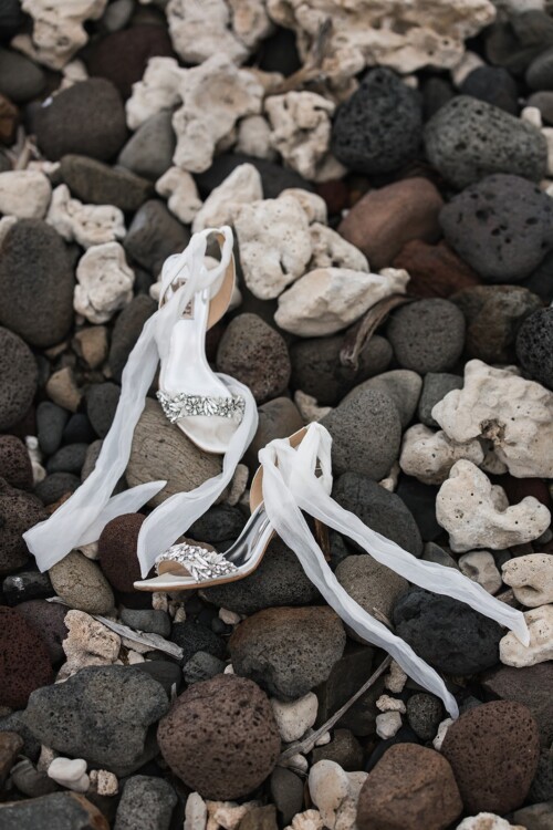 Matias Ezcurra Photography, Bridal heels with delicate ribbons rest on a rocky beach.