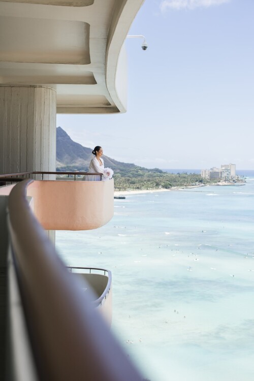 Matias Ezcurra Photography, Bride in white robe on luxury hotel balcony overlooking ocean, Kualoa Ranch wedding.