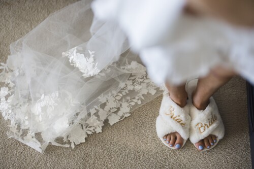 Matias Ezcurra Photography, Bride's feet in fluffy "Bride" slippers, next to her lace wedding veil.