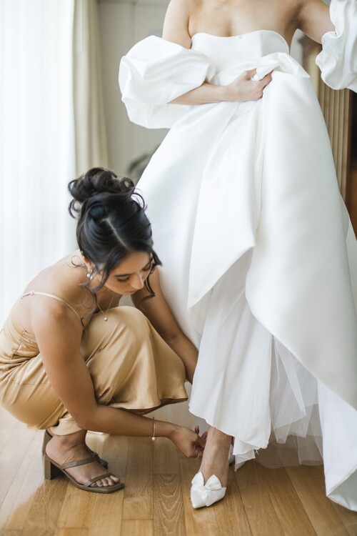 Matias Ezcurra Photography, Bride getting help putting on her wedding shoes at her Kualoa Ranch wedding.