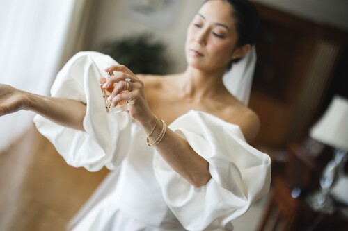 Matias Ezcurra Photography, Bride in white dress applying perfume at Kualoa Ranch wedding.