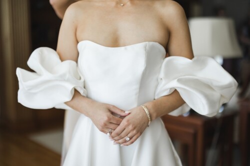 Matias Ezcurra Photography, Bride in strapless white wedding dress with large puffy sleeves, hands clasped. Kualoa Ranch wedding.