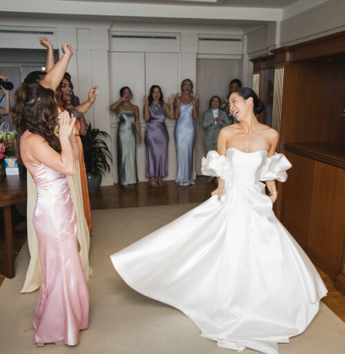 Matias Ezcurra Photography, Bride in white gown laughs with bridesmaids in pastel dresses at Kualoa Ranch wedding.