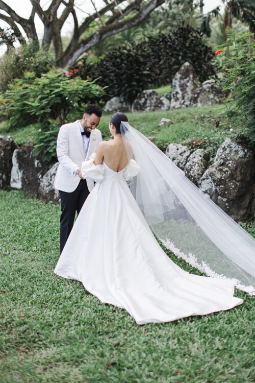 Matias Ezcurra Photography, Bride and groom share a first look at their Kualoa Ranch wedding. The bride wears a stunning off-the-shoulder gown with a long veil.