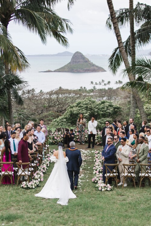 Matias Ezcurra Photography, Bride walking down the aisle at a Kualoa Ranch wedding ceremony with ocean view.