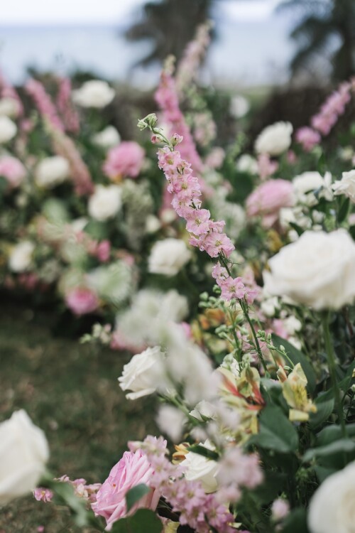 Matias Ezcurra Photography, Pink and white wedding flowers at a Kualoa Ranch ceremony. Roses, delphiniums, and other blooms create a lush floral arrangement.