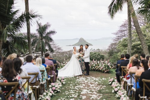 Matias Ezcurra Photography, Bride and groom exchange vows at a Kualoa Ranch wedding ceremony, with ocean and mountain views.