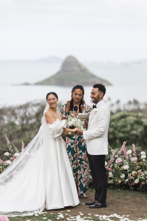 Matias Ezcurra Photography, Bride and groom exchange vows at a Kualoa Ranch wedding ceremony, officiated by a smiling officiant.