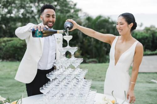 Matias Ezcurra Photography, Bride and groom pour champagne into a wedding champagne tower at their Kualoa Ranch wedding.