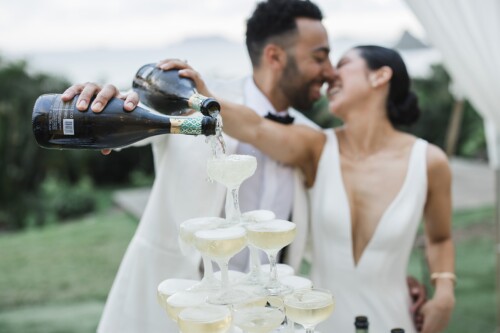 Matias Ezcurra Photography, Bride and groom pour champagne into a wedding champagne tower at their Kualoa Ranch wedding.