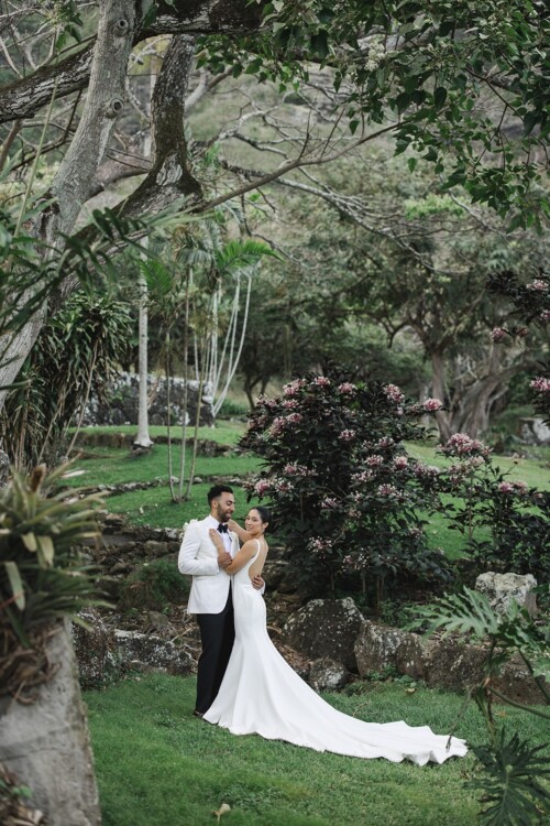 Matias Ezcurra Photography, Klaire & Alex embrace at their luxurious Kualoa Ranch wedding. The bride wears a stunning gown with a long train.