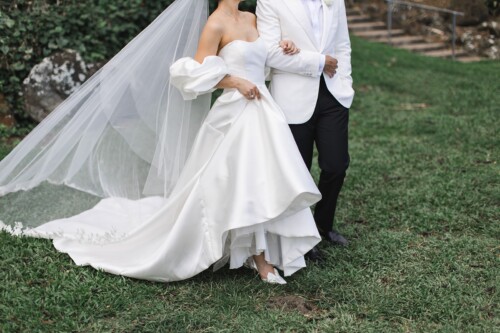 Matias Ezcurra Photography, Bride and groom walking at their Kualoa Ranch wedding. She wears a stunning white gown and veil.