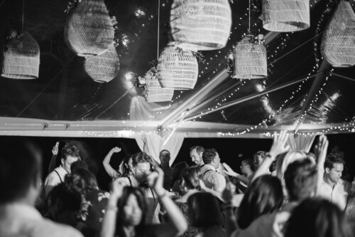 Matias Ezcurra Photography, Guests dance joyfully under wicker lanterns at a Kualoa Ranch wedding reception.