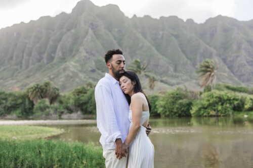 Matias Ezcurra Photography, Klaire and Alex embrace at their Kualoa Ranch wedding, stunning mountains in the background.