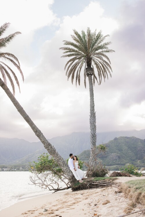 Matias Ezcurra Photography, Klaire & Alex embrace on a Kualoa Ranch beach, nestled by palm trees.